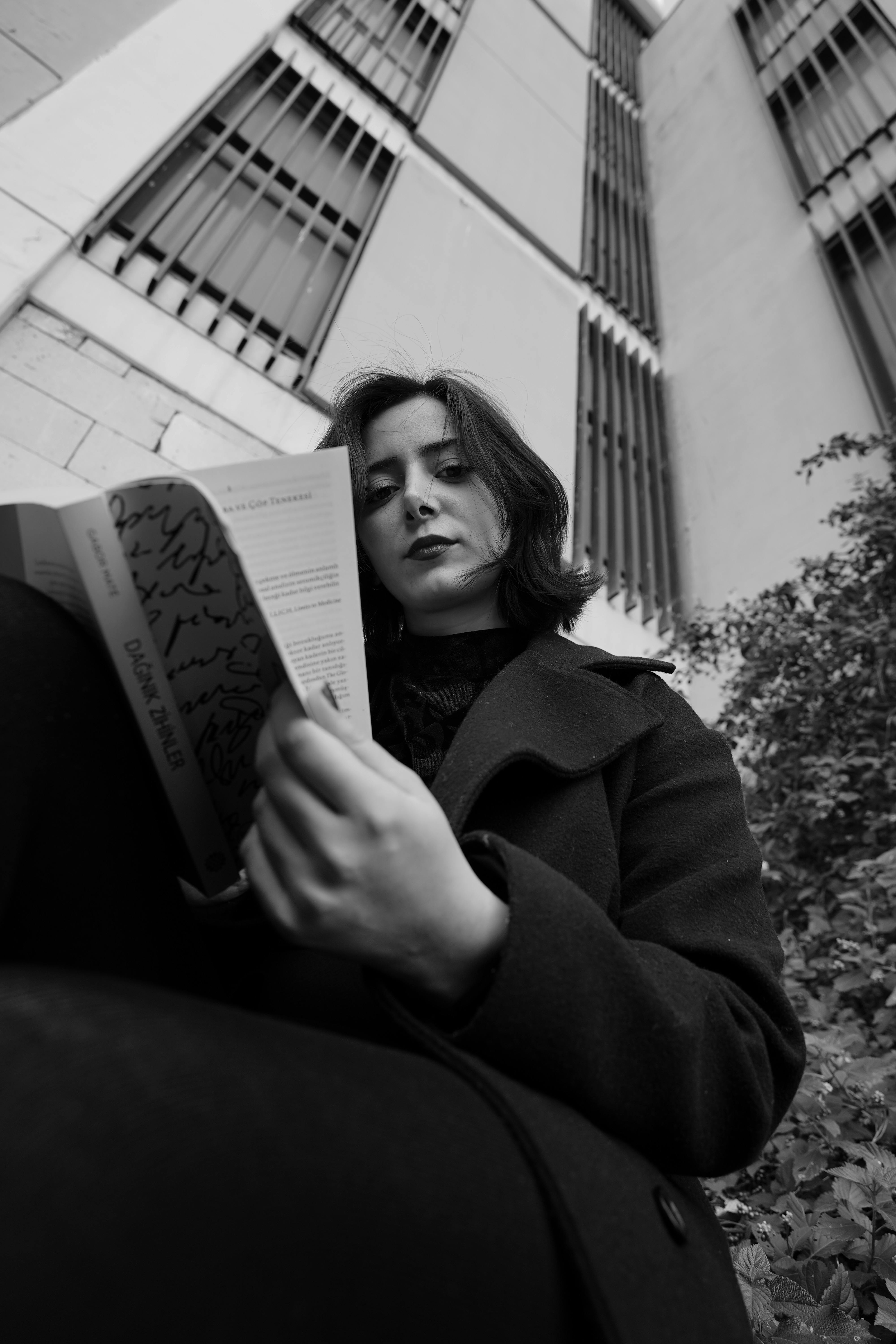 gratis Artistiek zwart-witportret van een vrouw in een jas die buiten een boek leest. Stockfoto