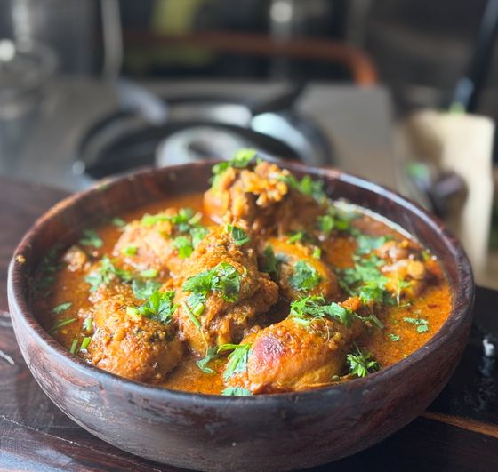 Bone-in chicken pieces in thick orange curry sauce with chopped cilantro in wooden bowl