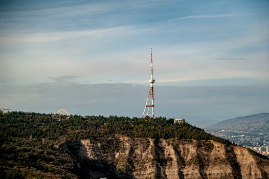 Vista spettacolare della Torre della TV di Tbilisi, in cima a una collina, circondata da una vegetazione lussureggiante e dal paesaggio urbano.