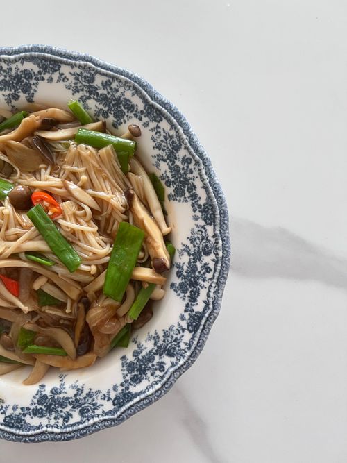 Free Top-down view of a mushroom stir fry served in a vintage-patterned dish on a white marble surface. Stock Photo