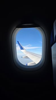View of blue sky and airplane wing through a plane window, ideal for travel themes.
