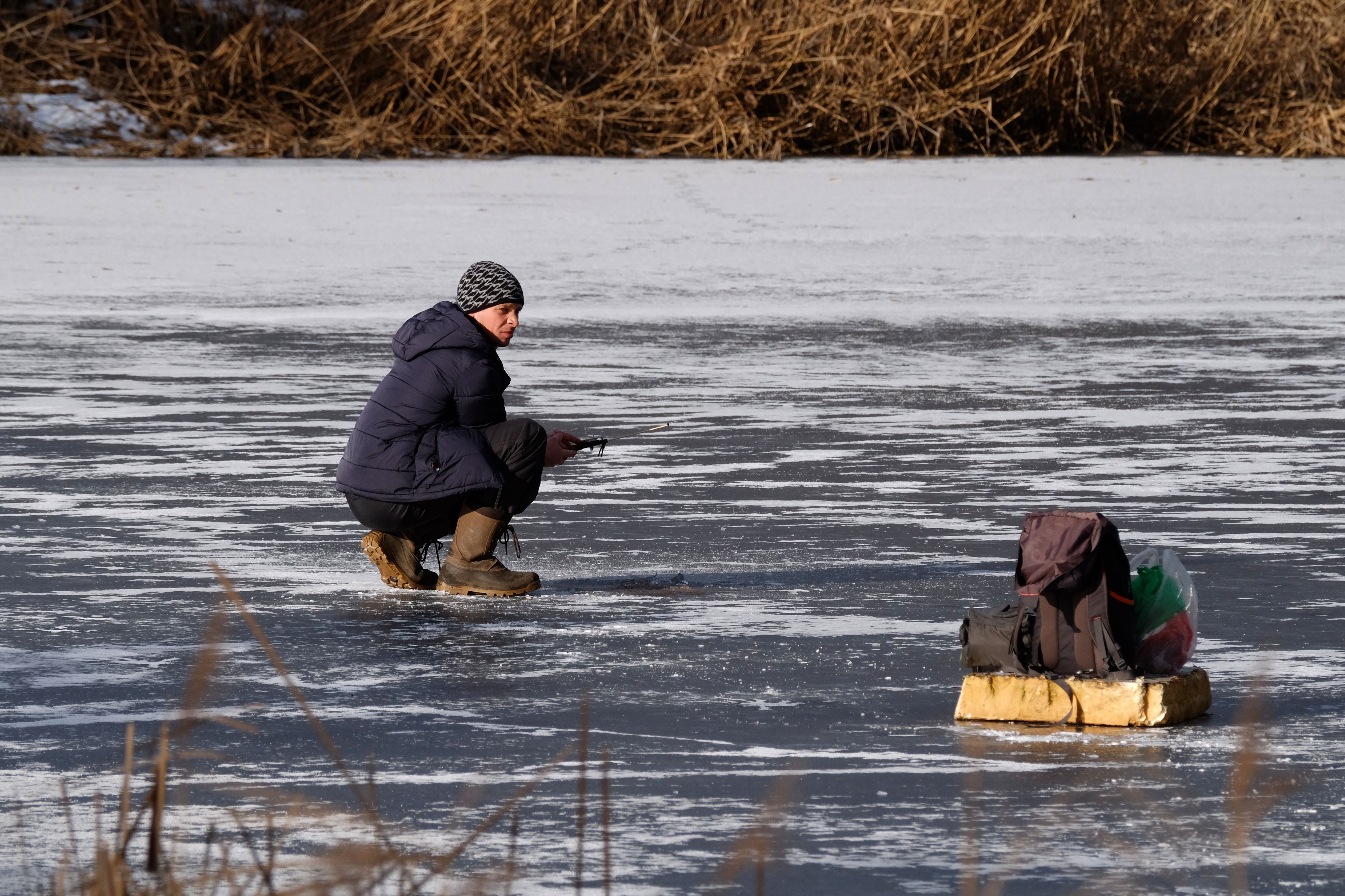 Man ice fishing on a frozen lake surrounded by winter scenery