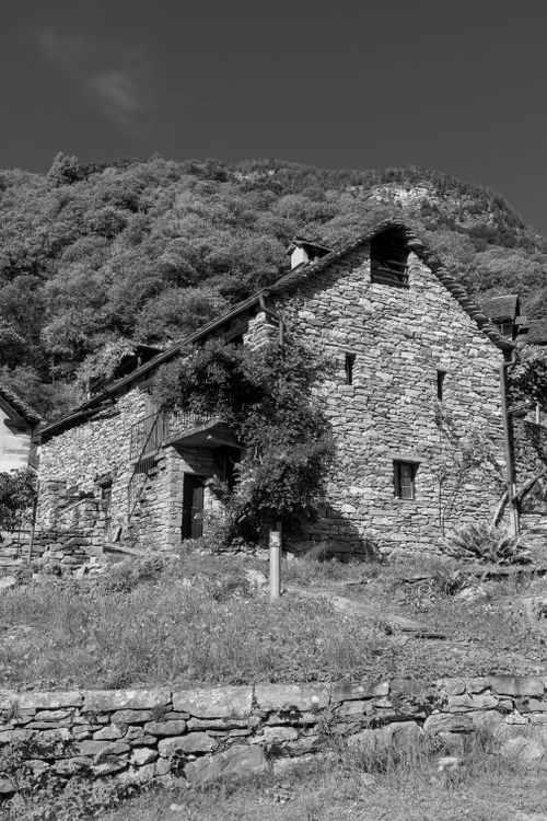 Free Black and white photo of a rustic stone house set against a hilly Swiss backdrop. Stock Photo
