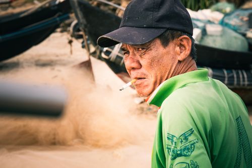 Free Middle-aged man smoking near fishing boats with an intense expression outdoors. Stock Photo