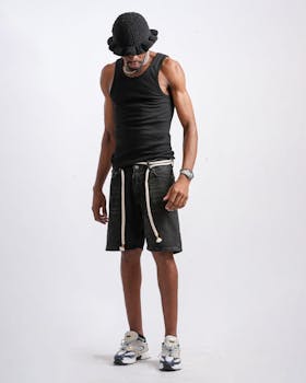 Fashionable man wearing a black tank top and denim shorts against white background.