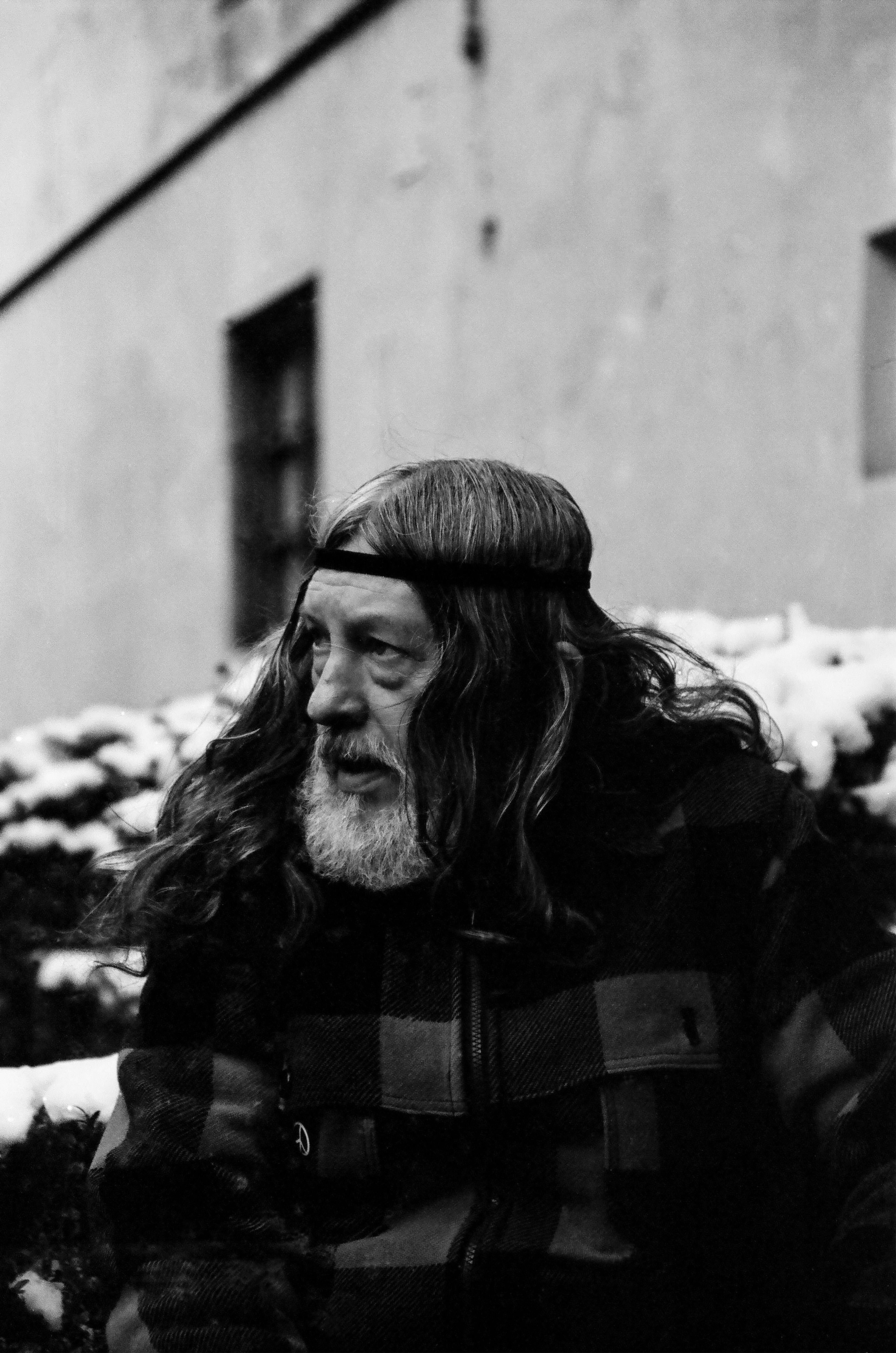 Thoughtful elderly man sitting outdoors in winter, wearing long hair and beard.