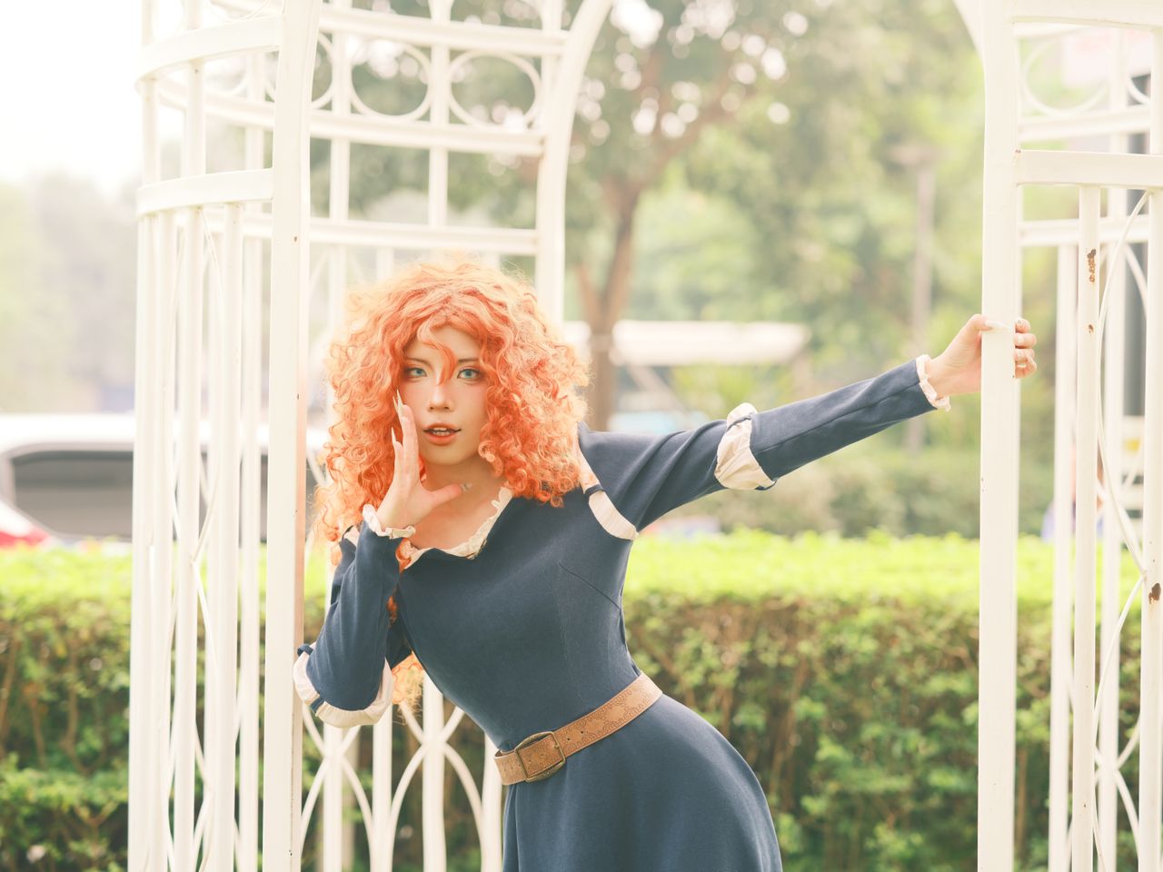 a cosplayer with curly hair poses in a stylish outfit outdoors on a su