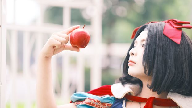 A person in Snow White cosplay holding a red apple outdoors, exuding a fairytale vibe.