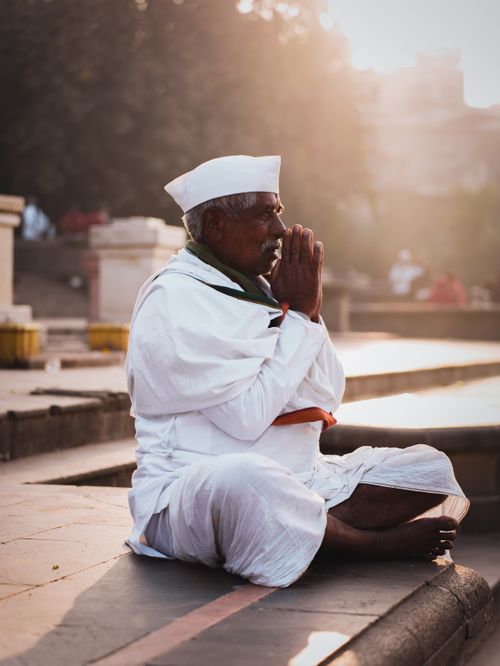 Free Elderly man in traditional attire praying by the river in Pune, India at sunrise. Stock Photo