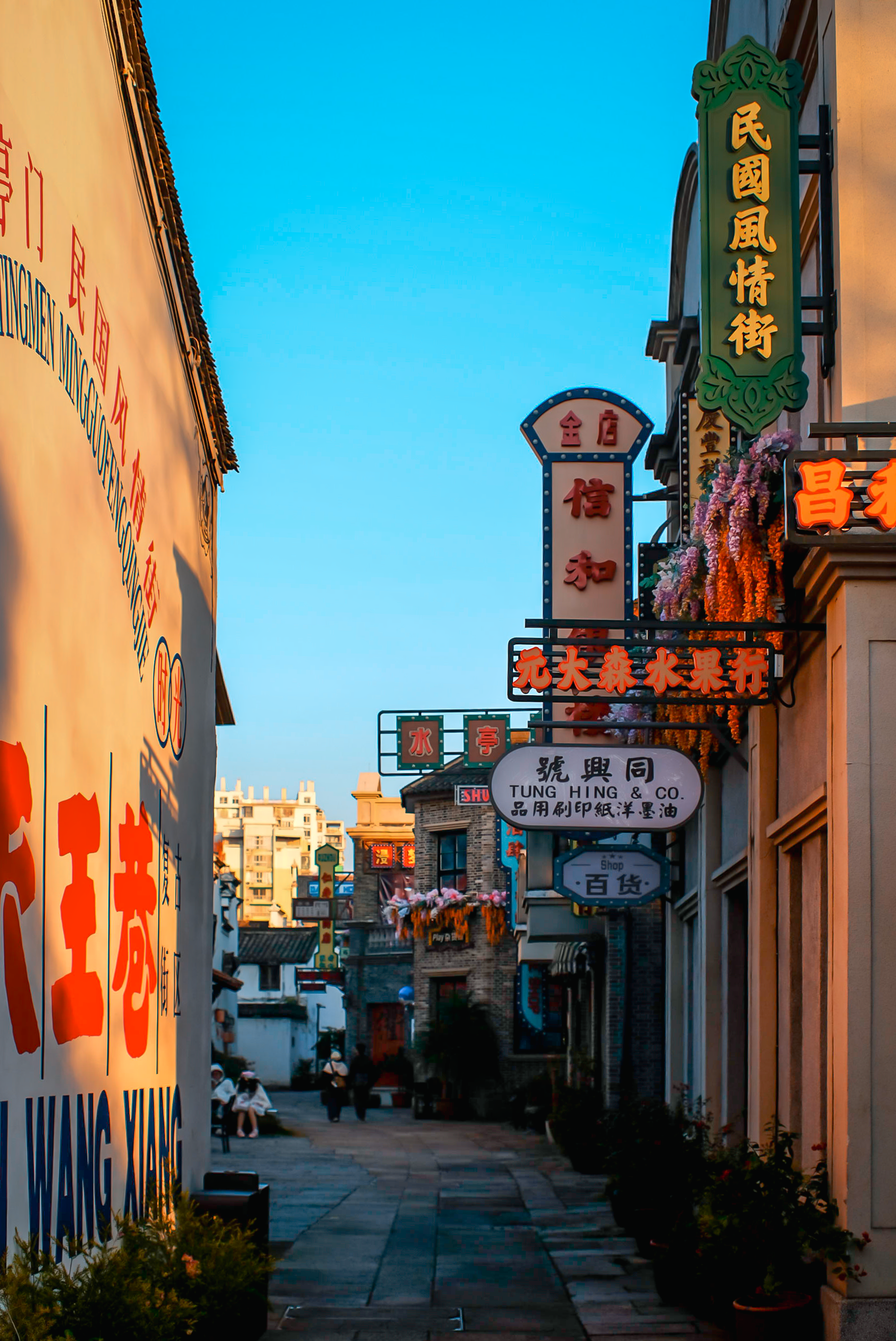 Vibrant signs line a narrow alley under a clear blue sky in a Chinese city.