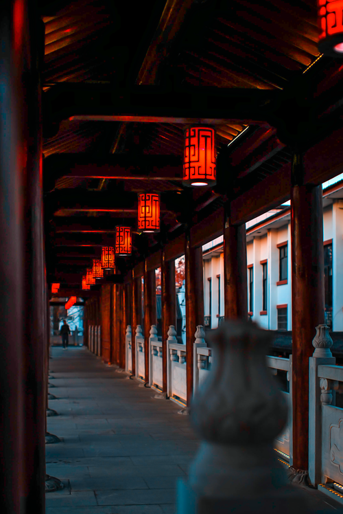 Free A row of red Chinese lanterns illuminates a traditional covered walkway at twilight. Stock Photo