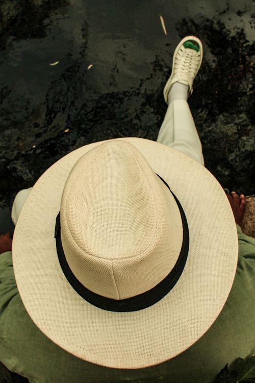 Free A person wearing a straw hat and sneakers relaxes by a body of water, viewed from above. Stock Photo