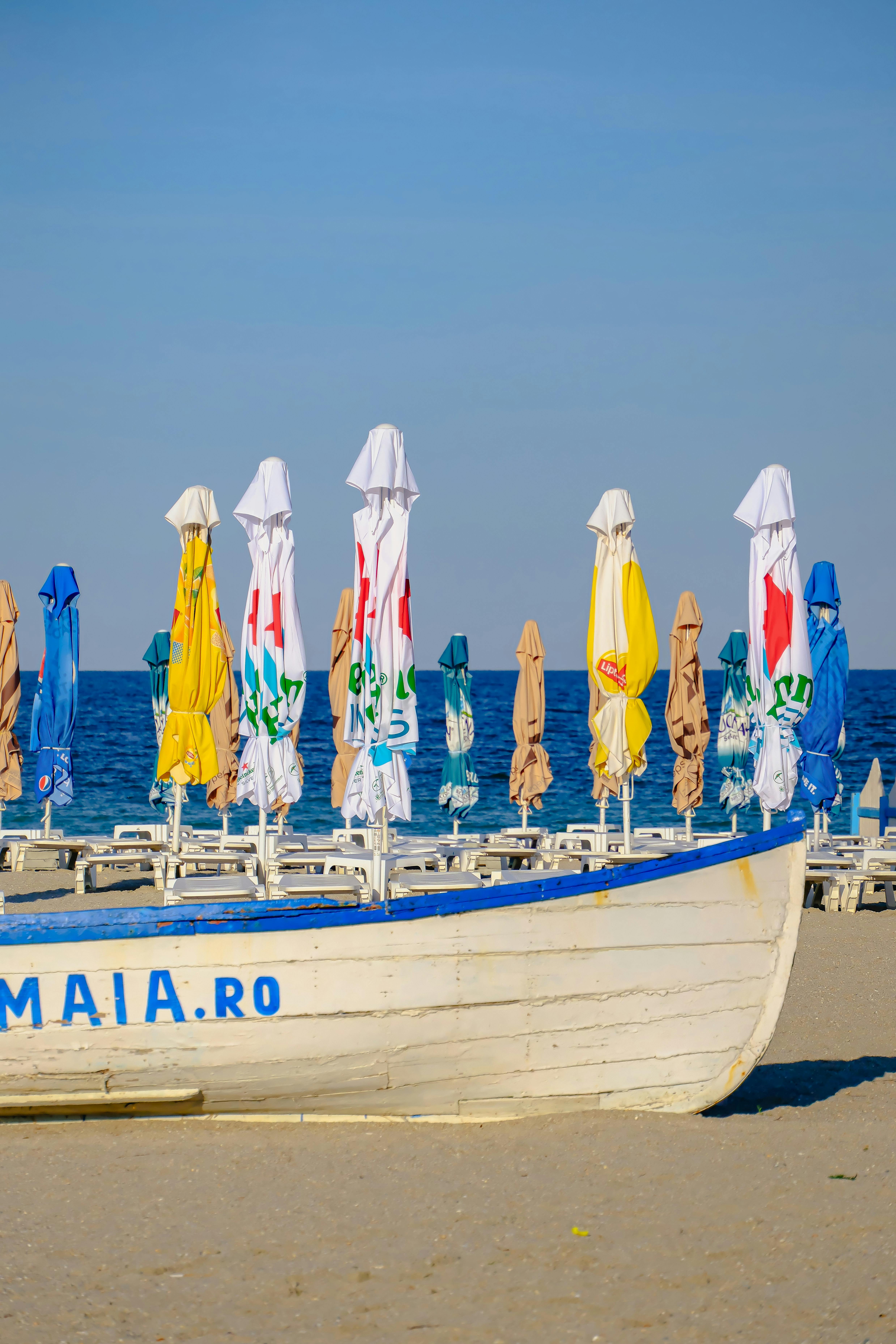 Vibrant umbrellas on a sandy beach with clear blue sea and sky, creating a serene and relaxed atmosphere.
