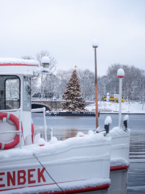 Free Snowy boat scene with a decorated Christmas tree by a river in Hamburg. Stock Photo