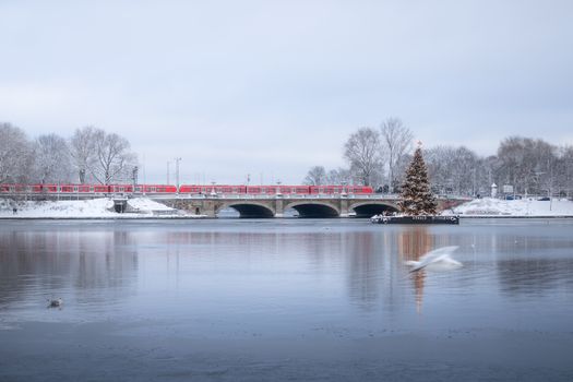 A serene winter landscape featuring a bridge, train, and Christmas tree in Hamburg's snowy setting.