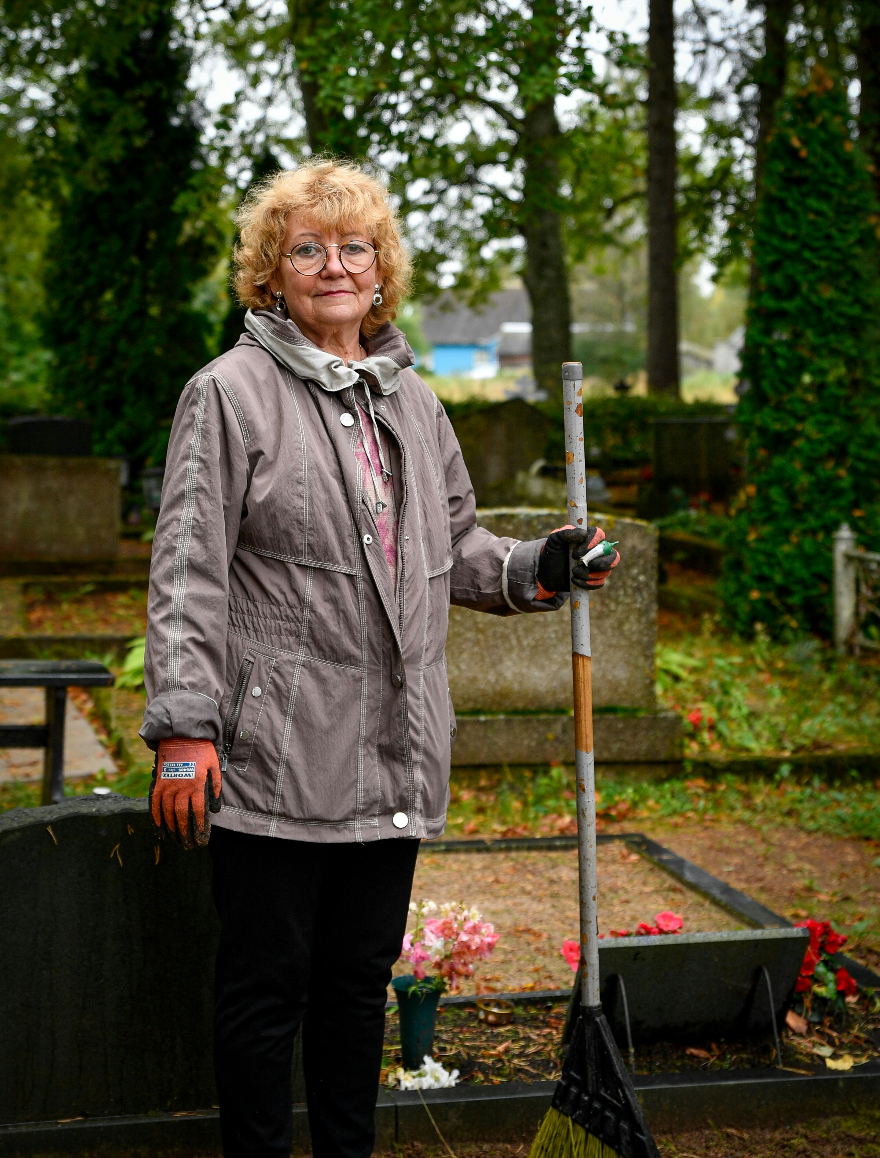 Senior woman maintaining a graveyard in Tartu County, Estonia during fall.