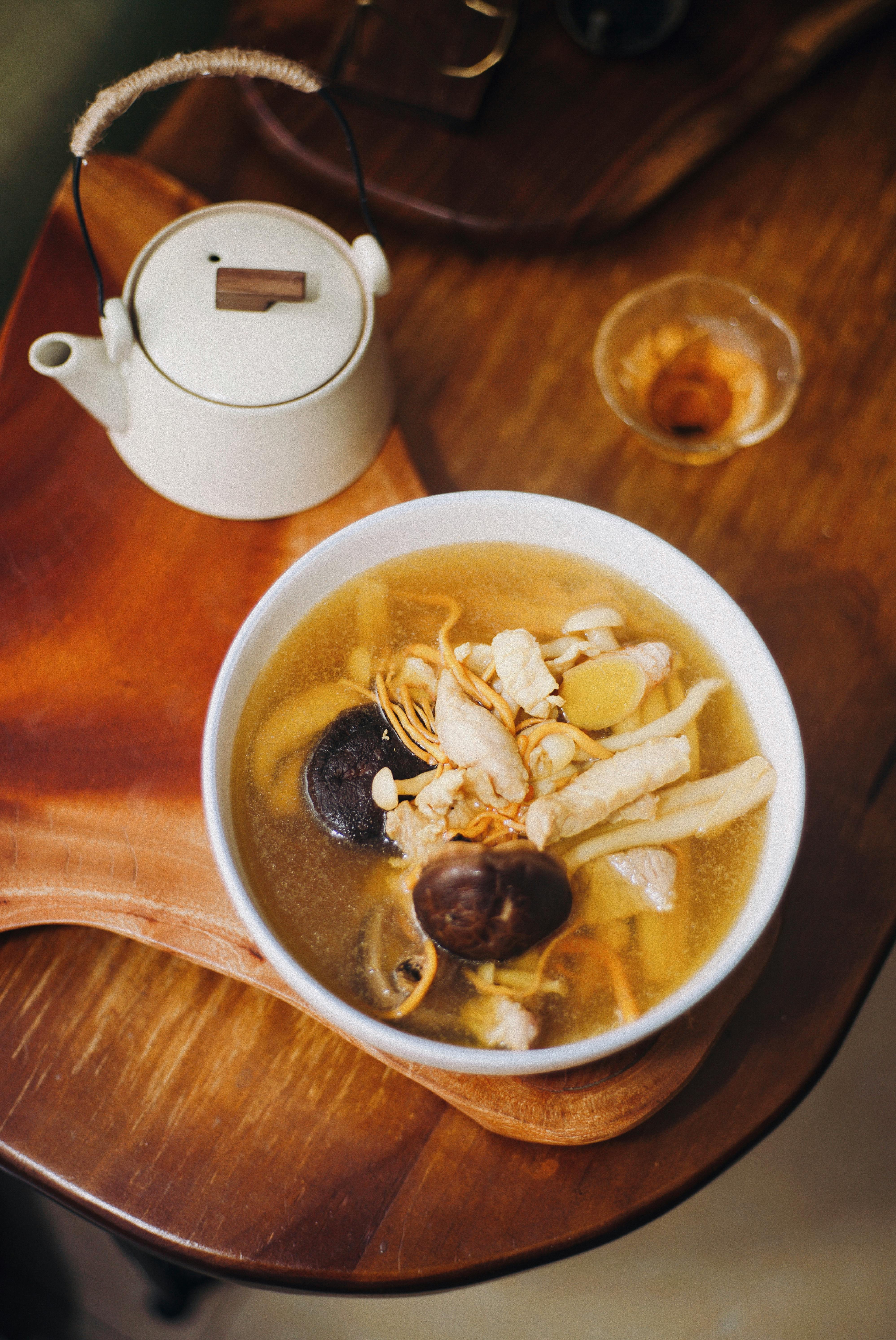 Warm Chinese chicken soup with mushrooms served on a wooden tray with a teapot.