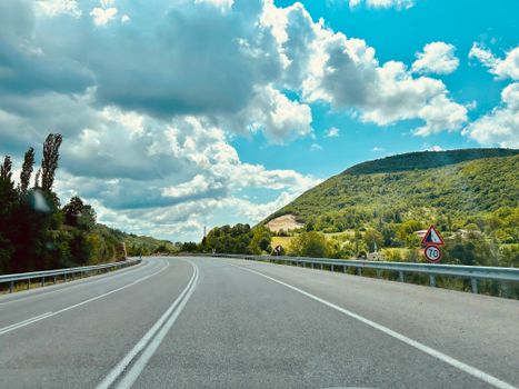 A picturesque highway winding through green hills under a bright blue sky with clouds.
