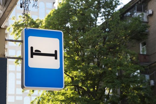 Hotel sign with bed symbol amidst urban greenery and buildings.