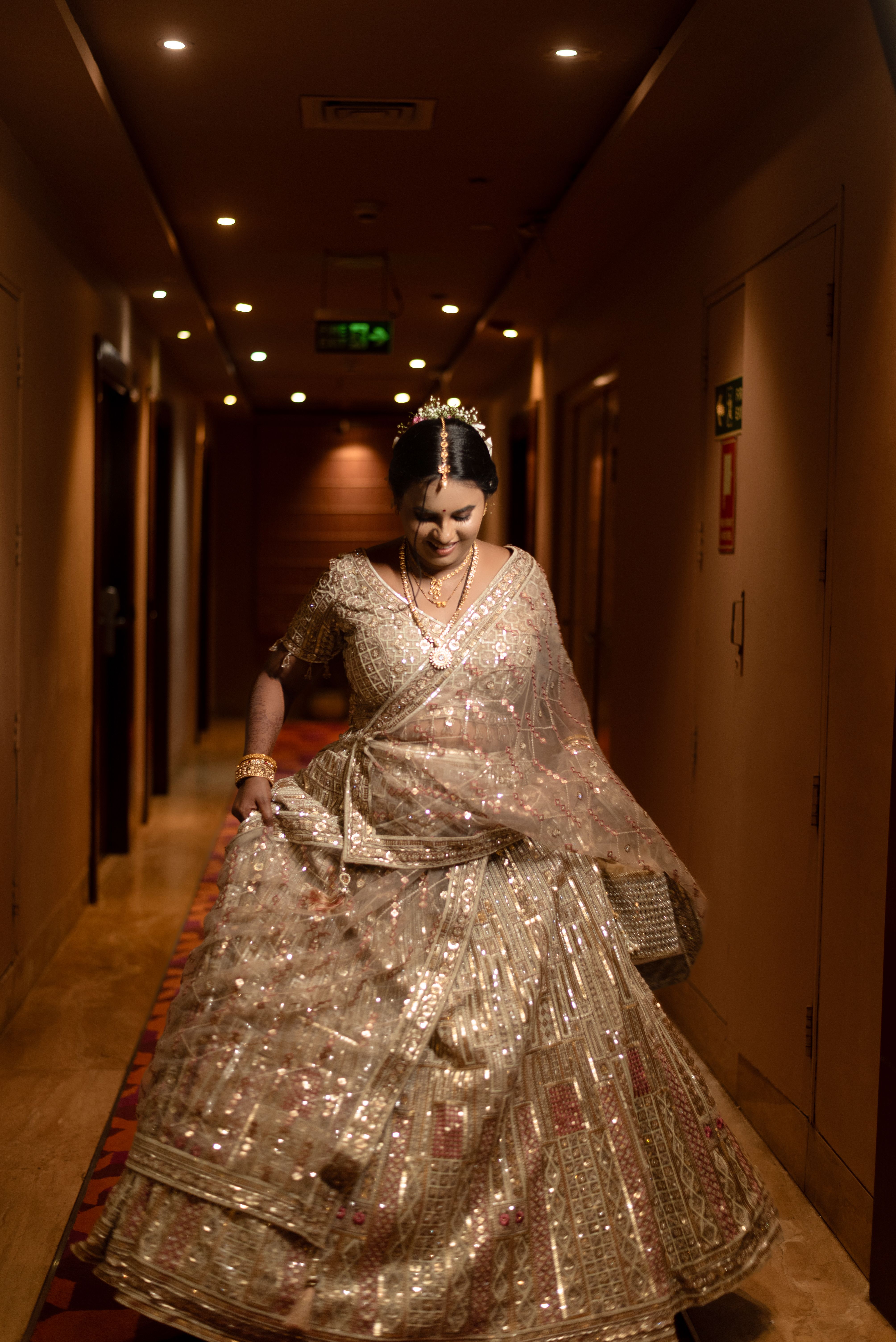 A stunning bride walking gracefully in a sparkling traditional Indian lehenga indoors.
