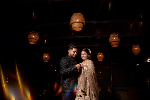 A beautifully dressed couple shares a romantic moment at an Indian wedding under warm ambient lighting.