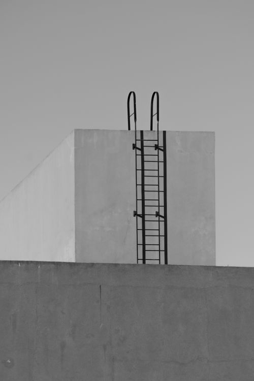 Free Black and white image of a solitary industrial ladder against a minimalist abstract building structure. Stock Photo