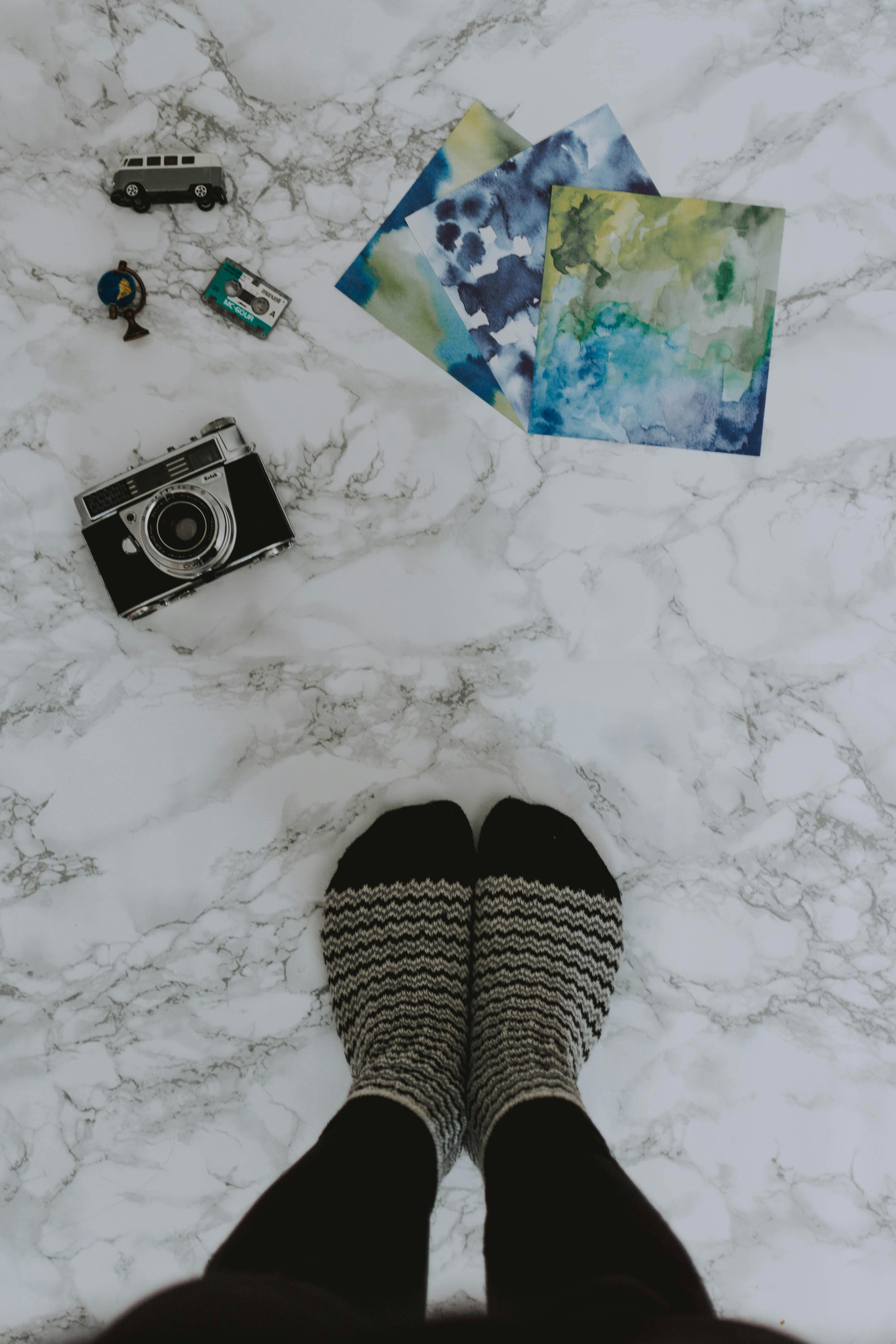 老式相机、艺术印刷品、玩具车和大理石表面上穿着袜子的脚的俯视图