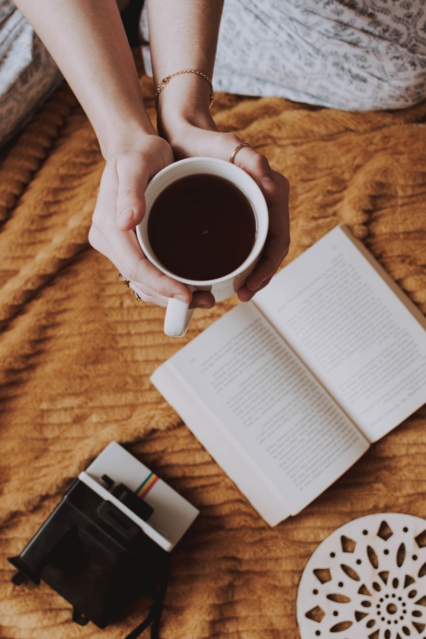 Woman holding coffee beside an open book in warm morning light