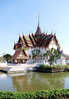 Beautiful Thai temple with ornate roof reflecting in the water under a clear blue sky.