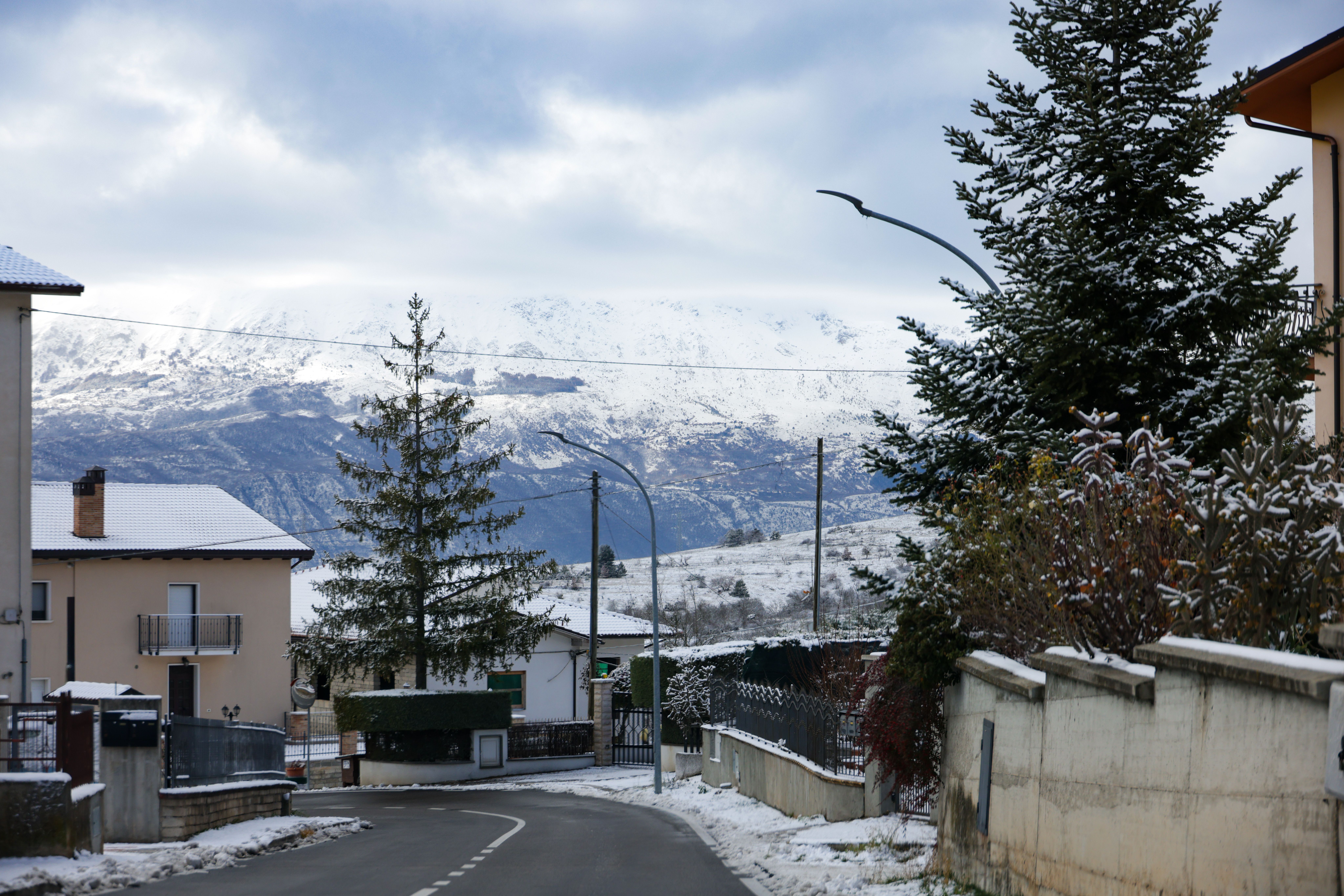 Scenic snow-covered village road with mountain backdrop under a cloudy winter sky.