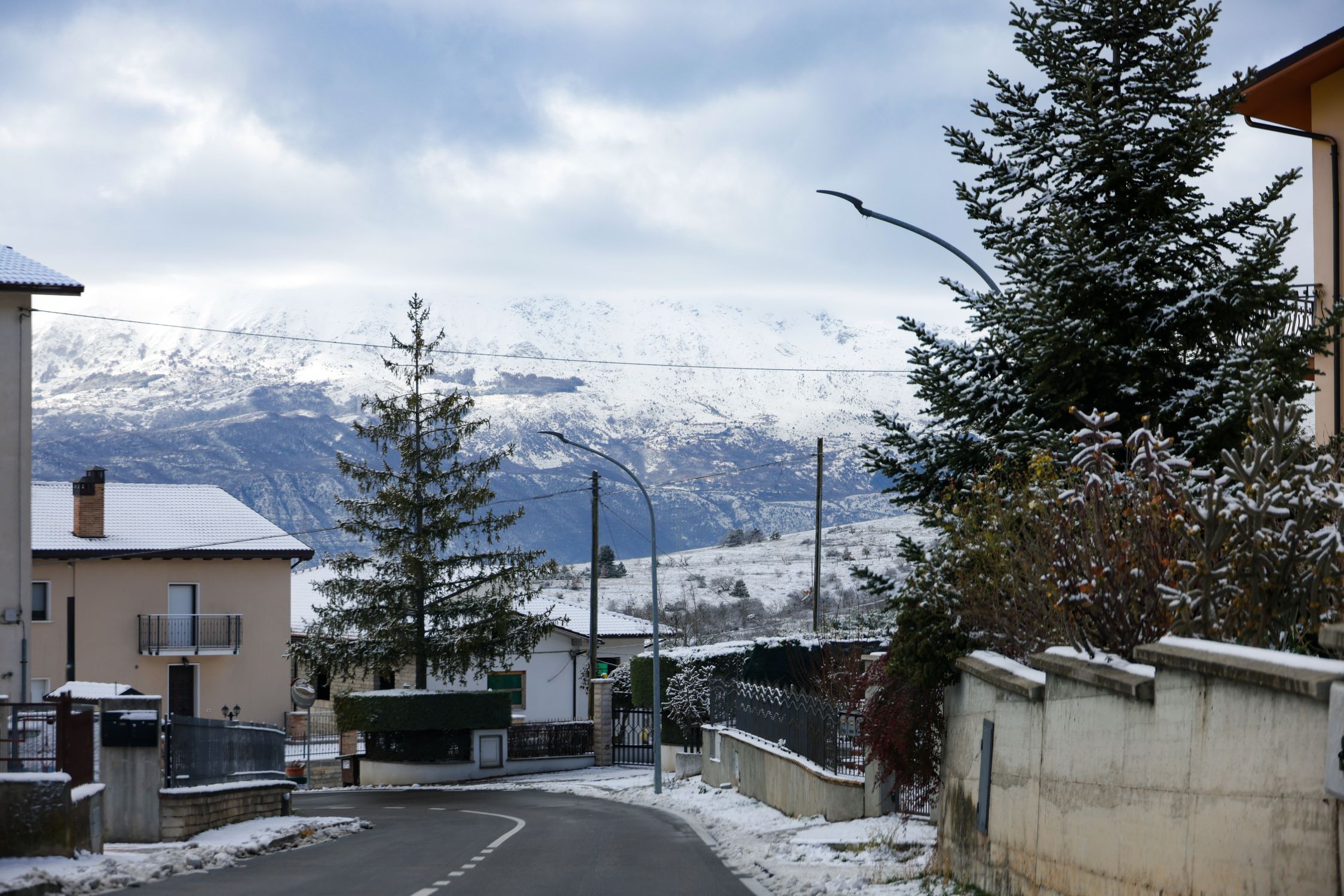 Scenic snow-covered village road with mountain backdrop under a cloudy winter sky.