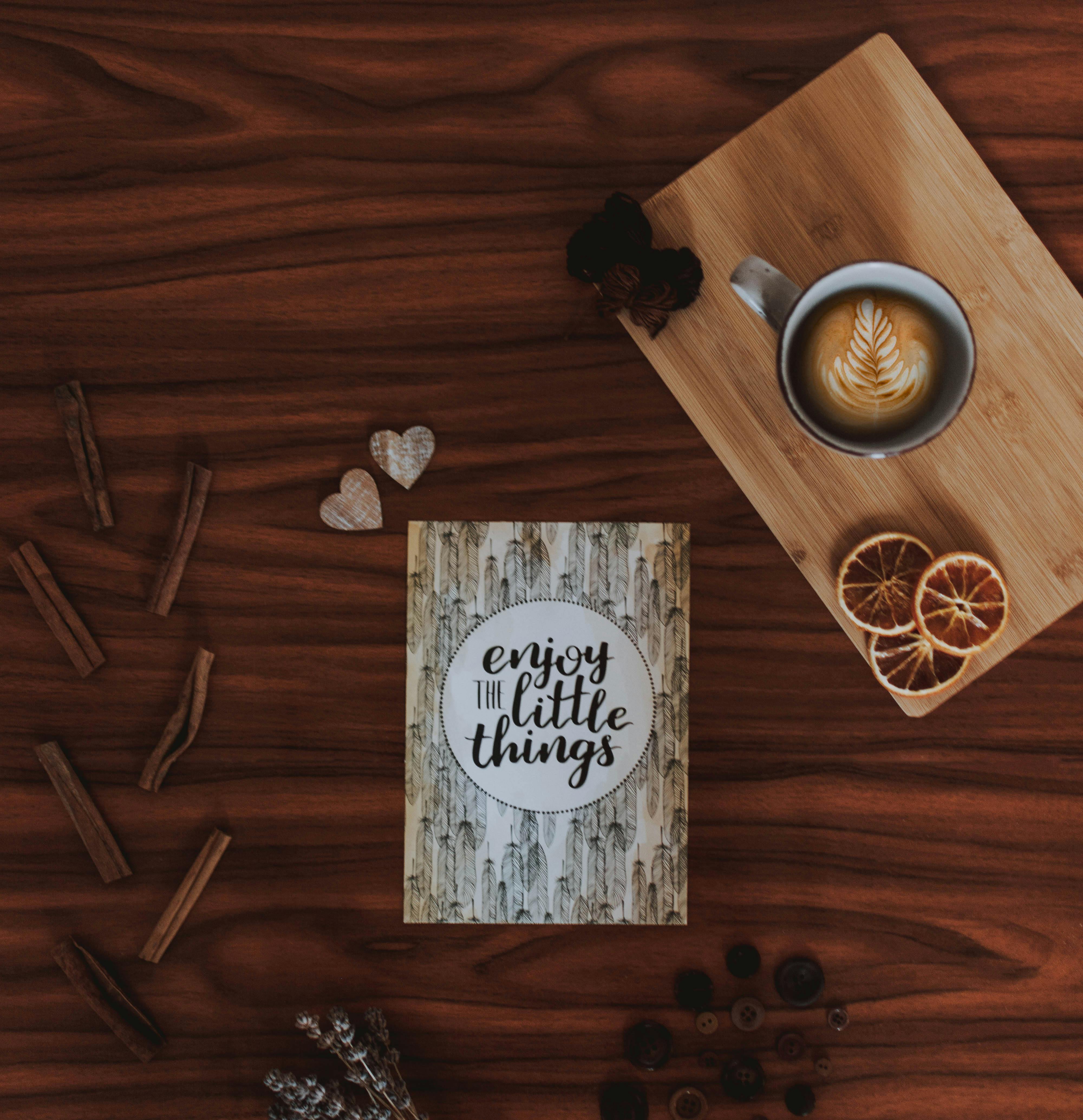 在木制表面上，一杯平淡的咖啡、一点肉桂和一句名言，提醒我们“享受小东西”