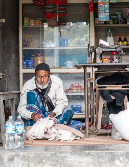 Free An elderly man sits sewing clothes in a small shop filled with various items. Traditional setting. Stock Photo