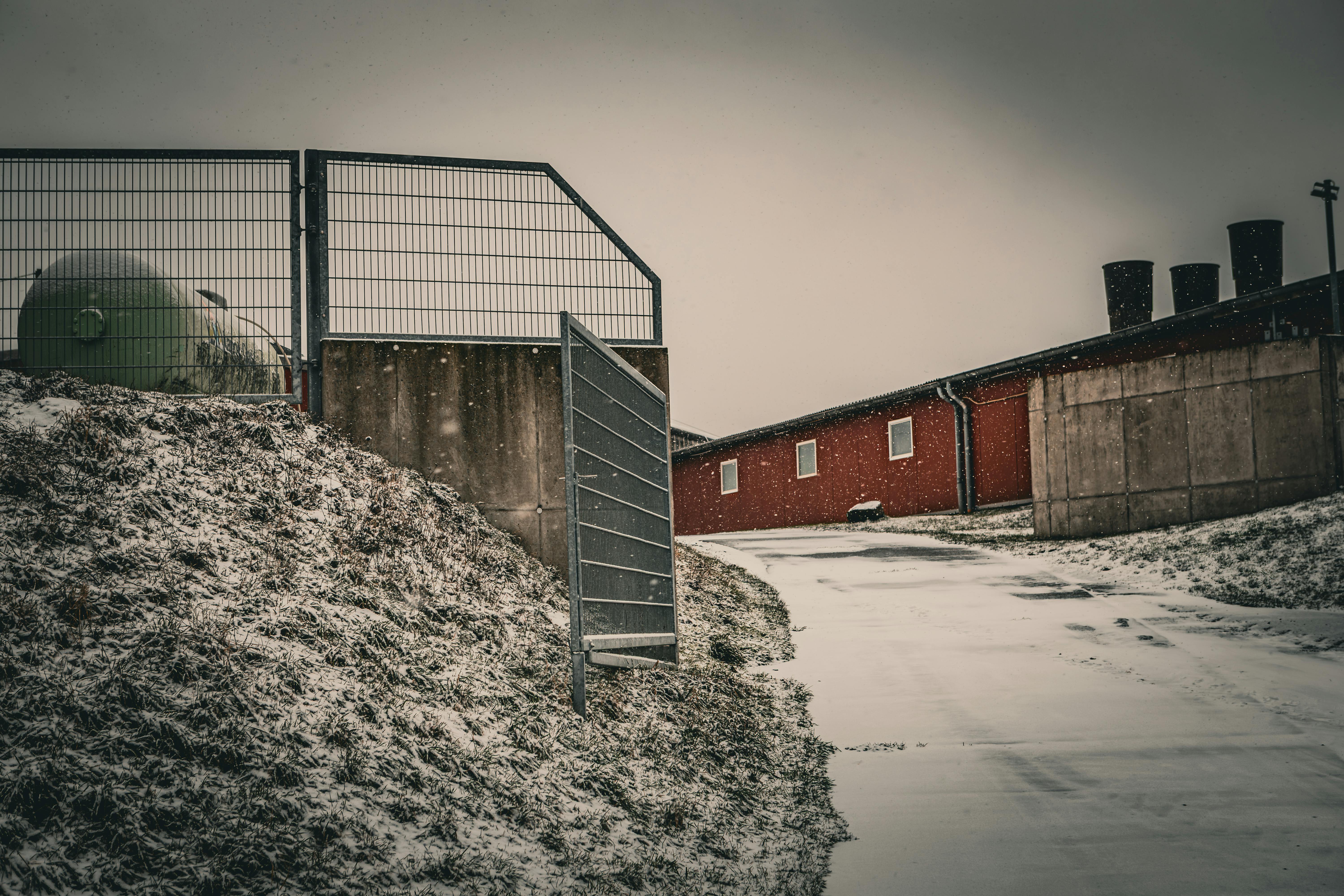 Snow-covered industrial yard with red buildings and a metal structure on the left.