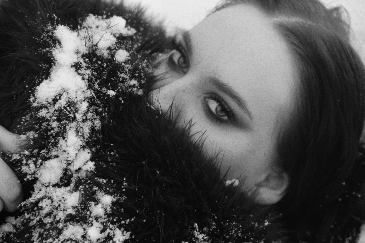 black and white close up portrait of a woman with snow on fur gazing i