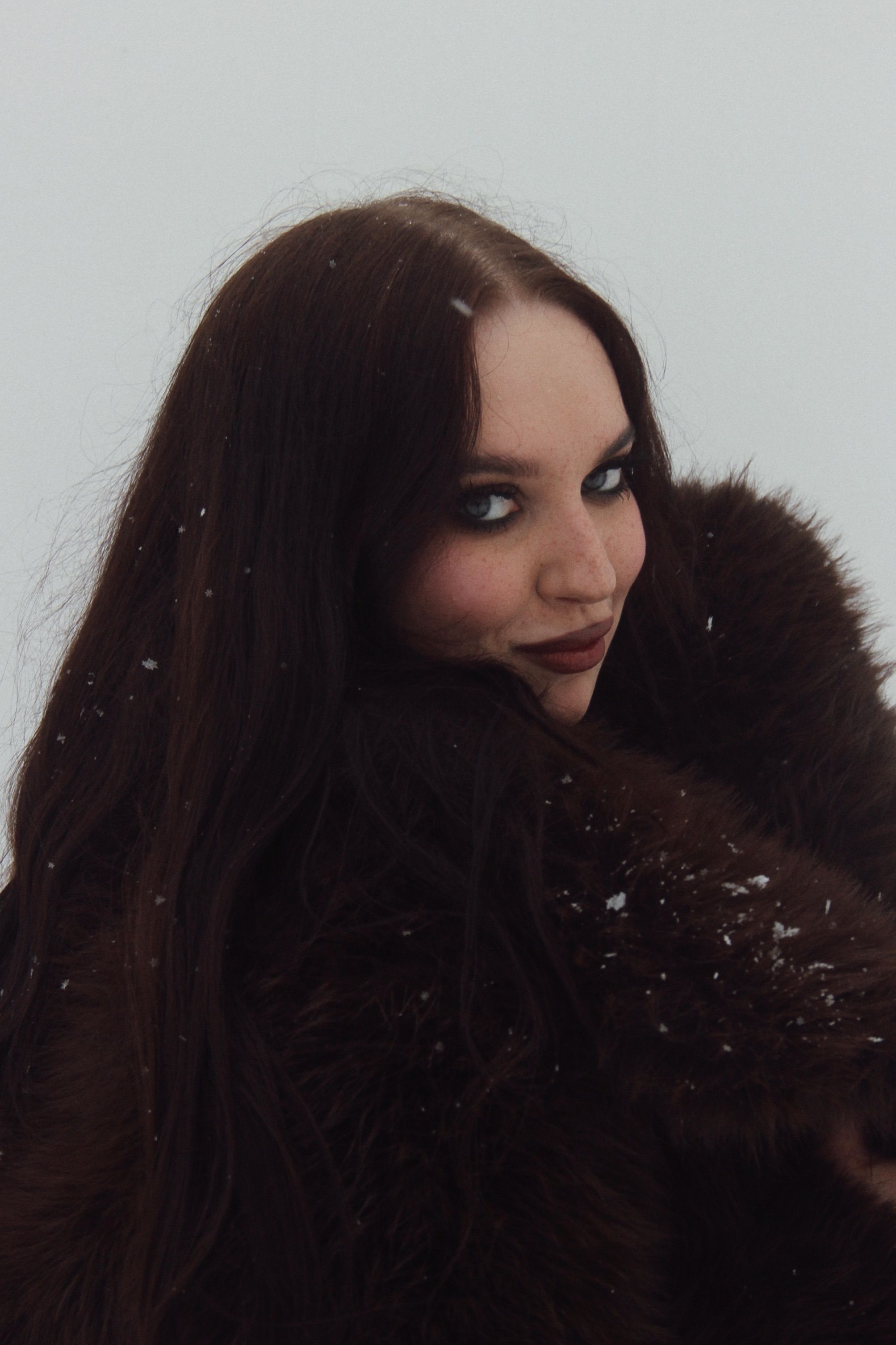 Portrait of a woman in a fur coat with snowy background, exuding glamor.