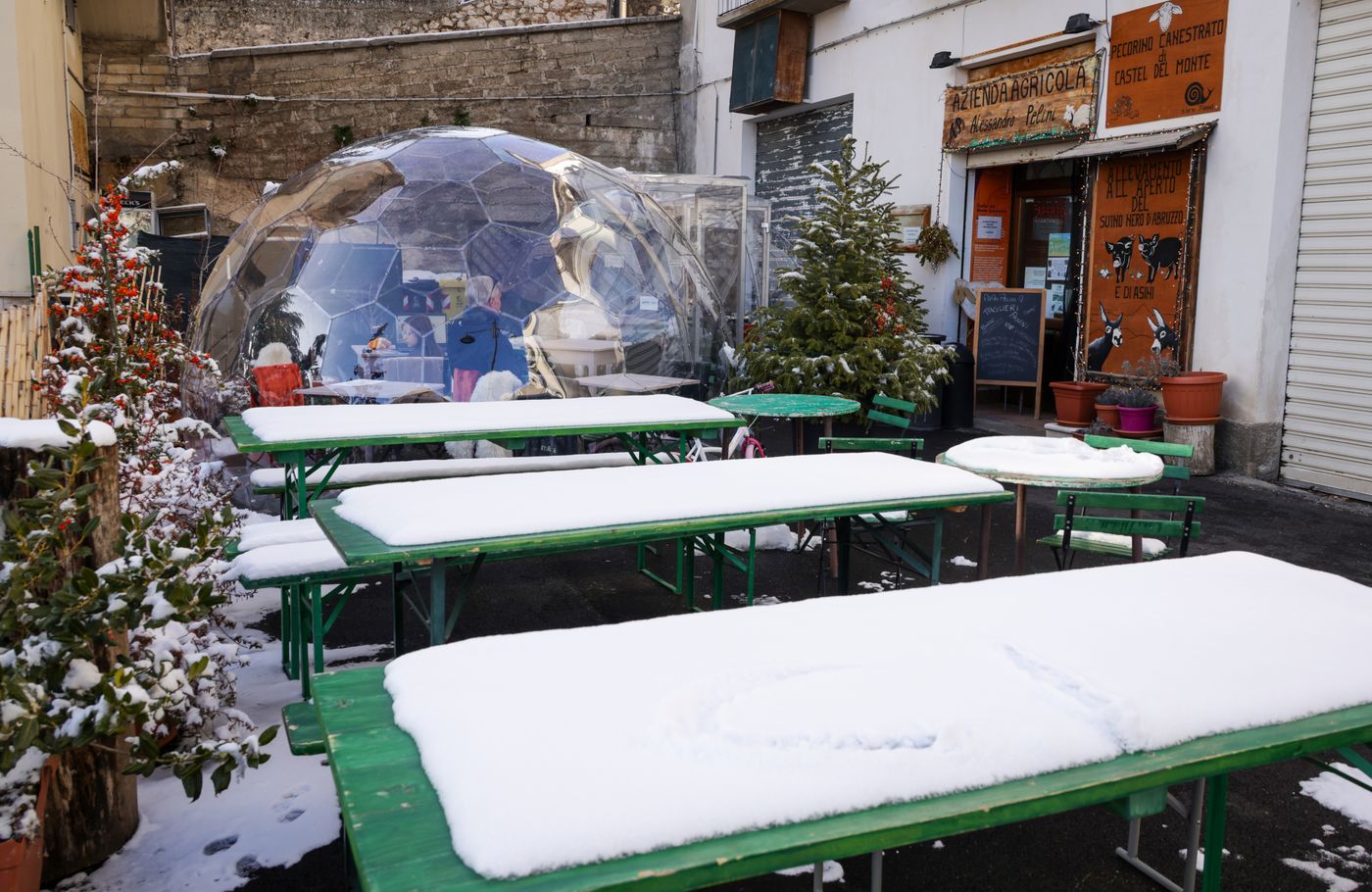A clear transparent dome shelter with seating inside, standing in snow.