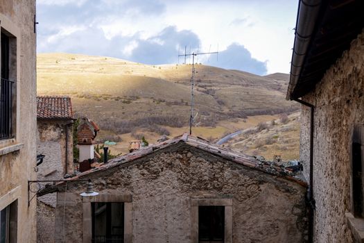 Rustic Italian village with stone buildings and scenic hills under a bright sky.