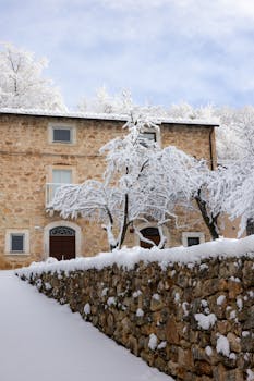 A beautiful stone house surrounded by snow-covered trees and a stone wall.