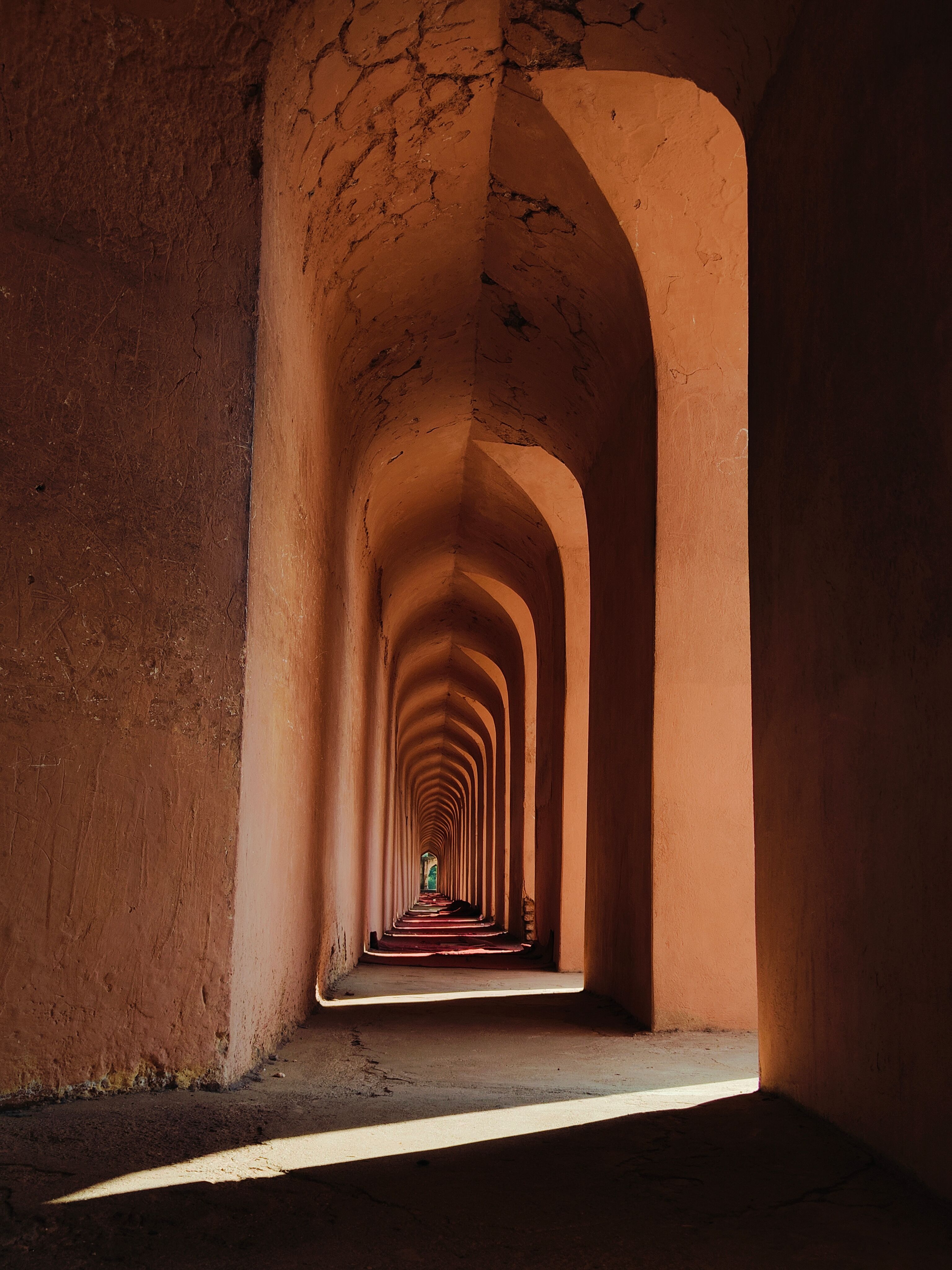 Gratuit Une personne se tient au bout d'un long couloir d'arcades baignées de soleil, créant une atmosphère mystérieuse. Photos