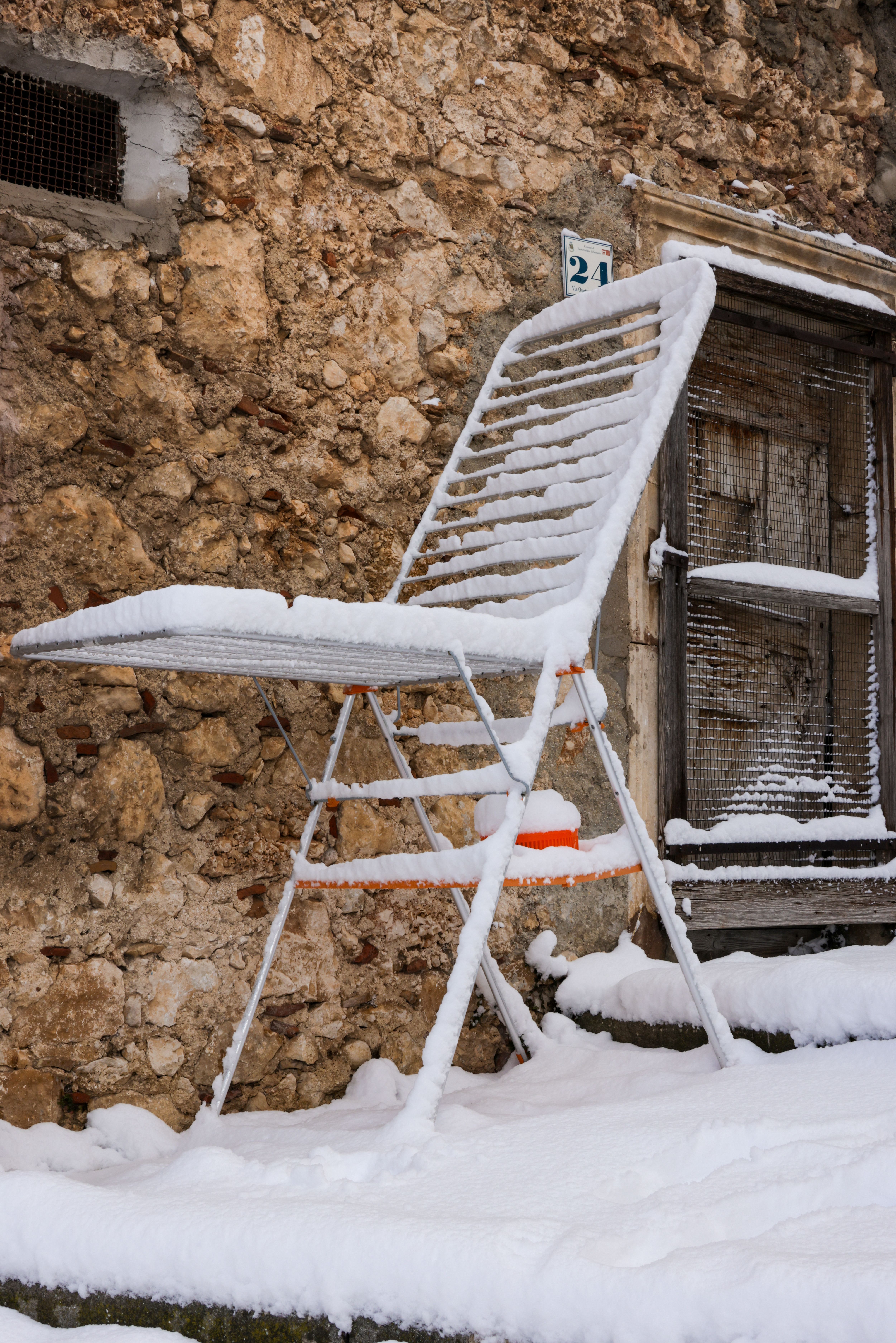 A snow-covered folding chair against a rustic stone wall, capturing winter's charm.