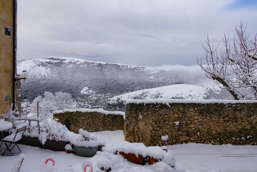 Free Scenic winter view of snow-covered mountains and a stone wall under a cloudy sky. Stock Photo