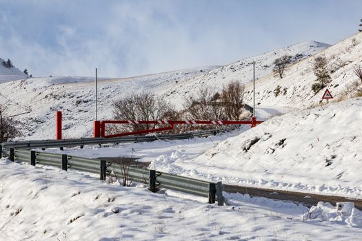 Snow-covered mountain road with red barrier, capturing a serene winter landscape.
