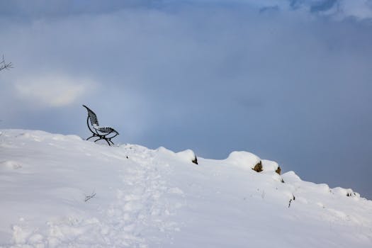 A solitary metal bench on a snow-covered hill under a cloudy sky, exuding peace and solitude.
