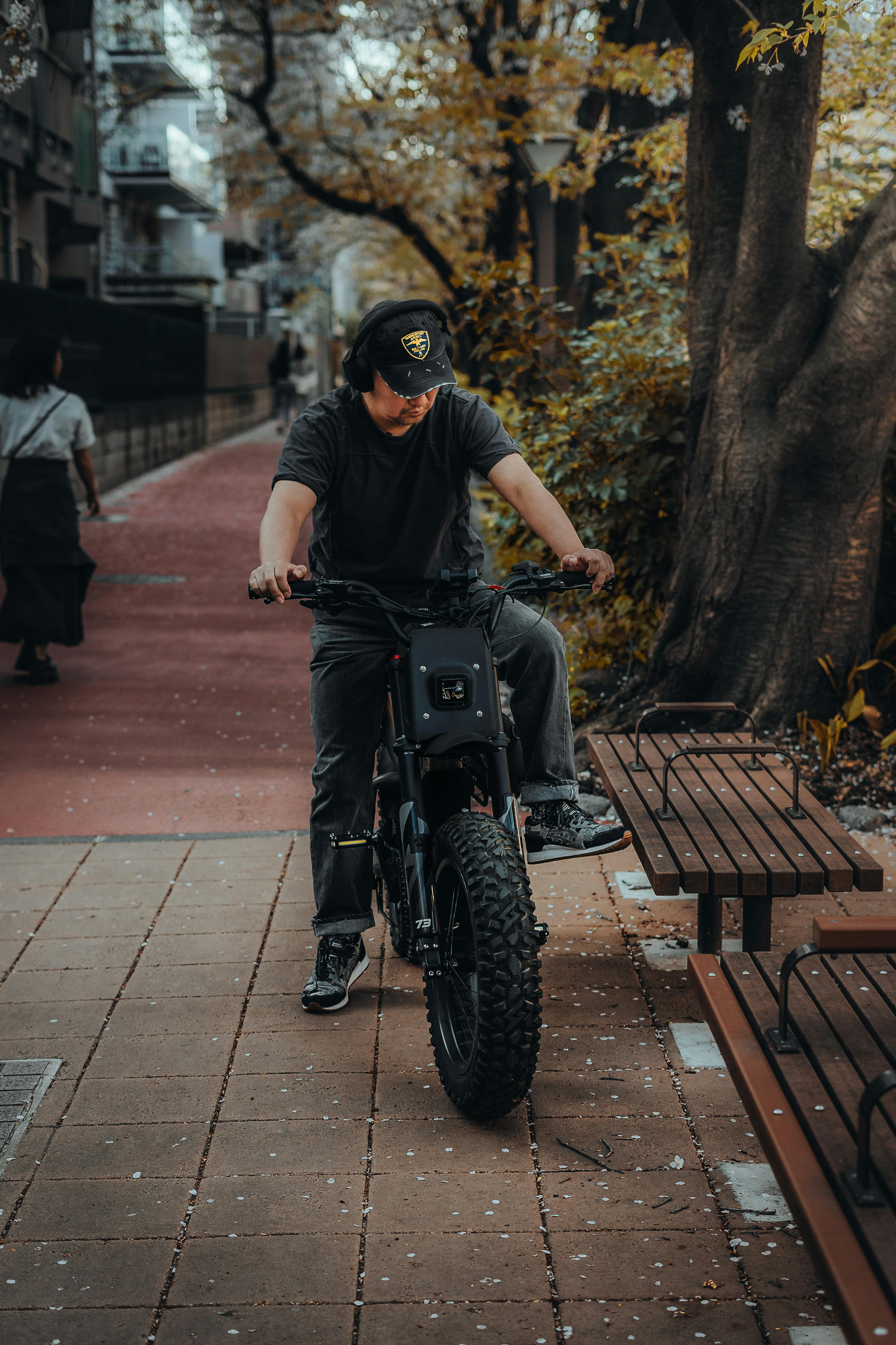 A person rides a black electric motorbike on a park pathway surrounded by trees.