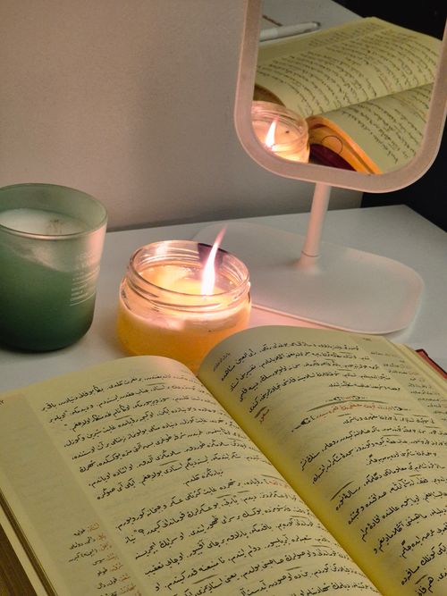 Free A cozy setup with an open book, candles, and a mirror reflecting warm candlelight. Stock Photo