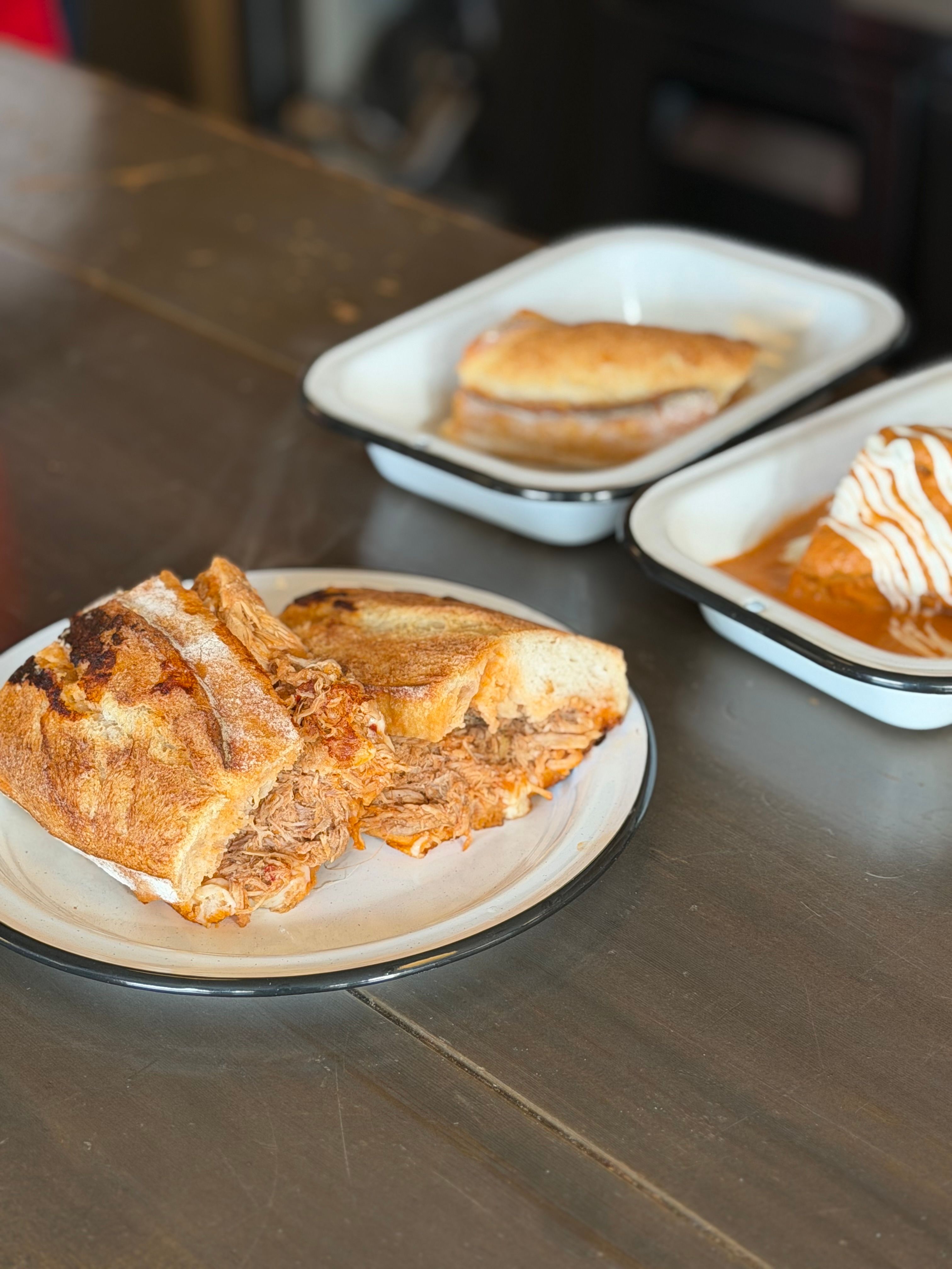 A pressed Cuban sandwich sliced diagonally on a cutting board, showing layers of roast pork, ham, melted Swiss cheese, and pickle slices between golden, crisscross-marked bread.
