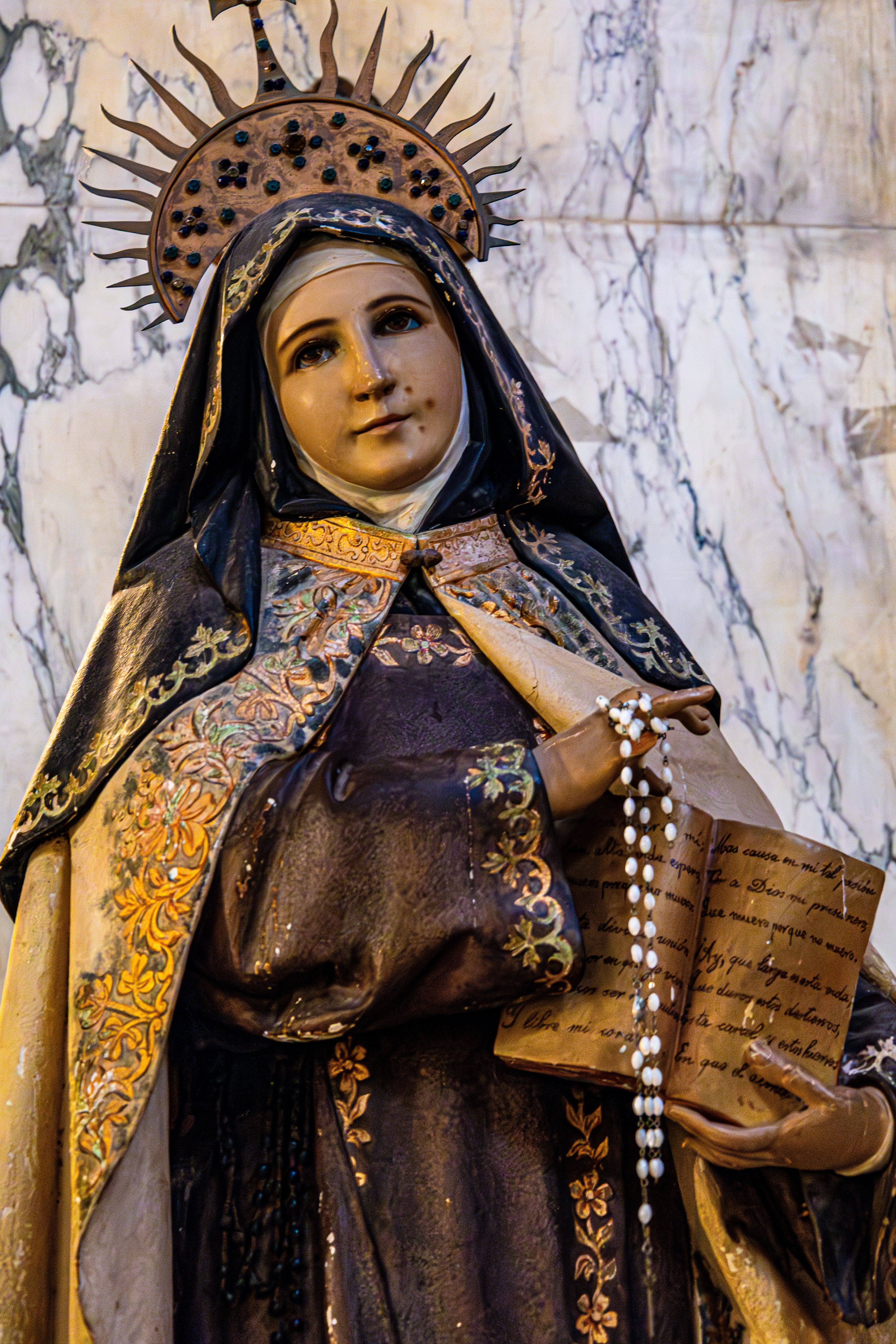 Statue of a saint holding rosary and book inside a Haifa church.