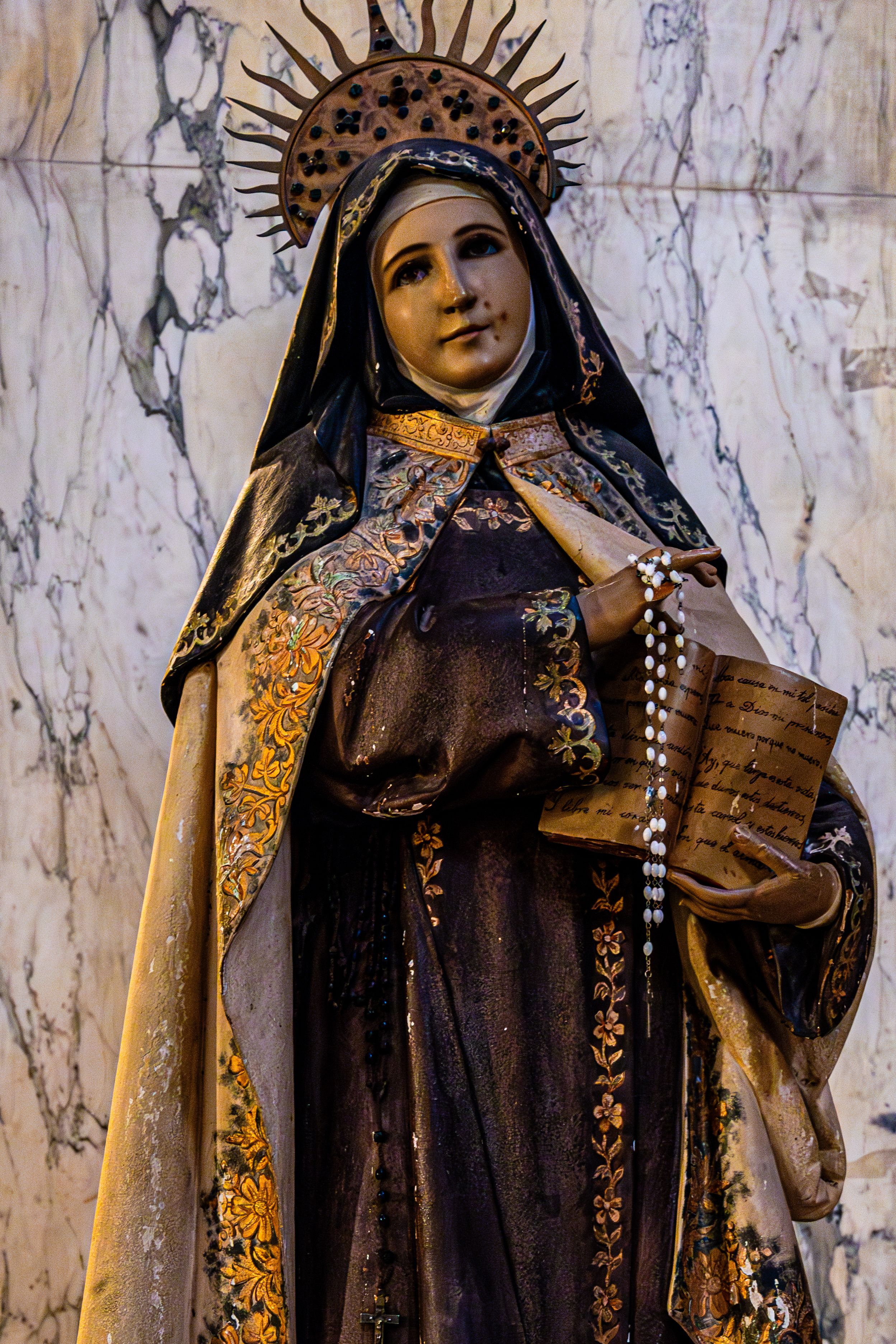 Detailed statue of a saint in ornate robes indoors with marble backdrop.