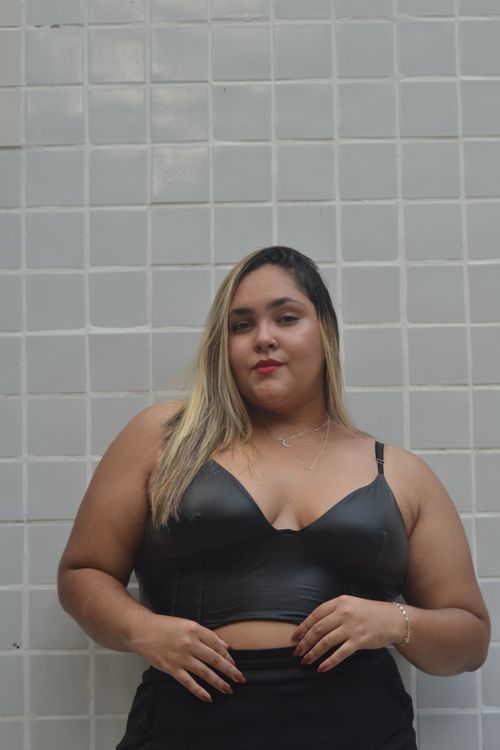 Free Portrait of a confident young woman in a sleek black top against a tiled wall. Stock Photo